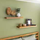 Solid wood floating shelves TUUL on a green bedroom wall decorated with a plant, candle and a photo frame.