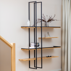 Solid wood floating shelf PÄIKE with two metal frames on a living room wall decorated with a plant and books