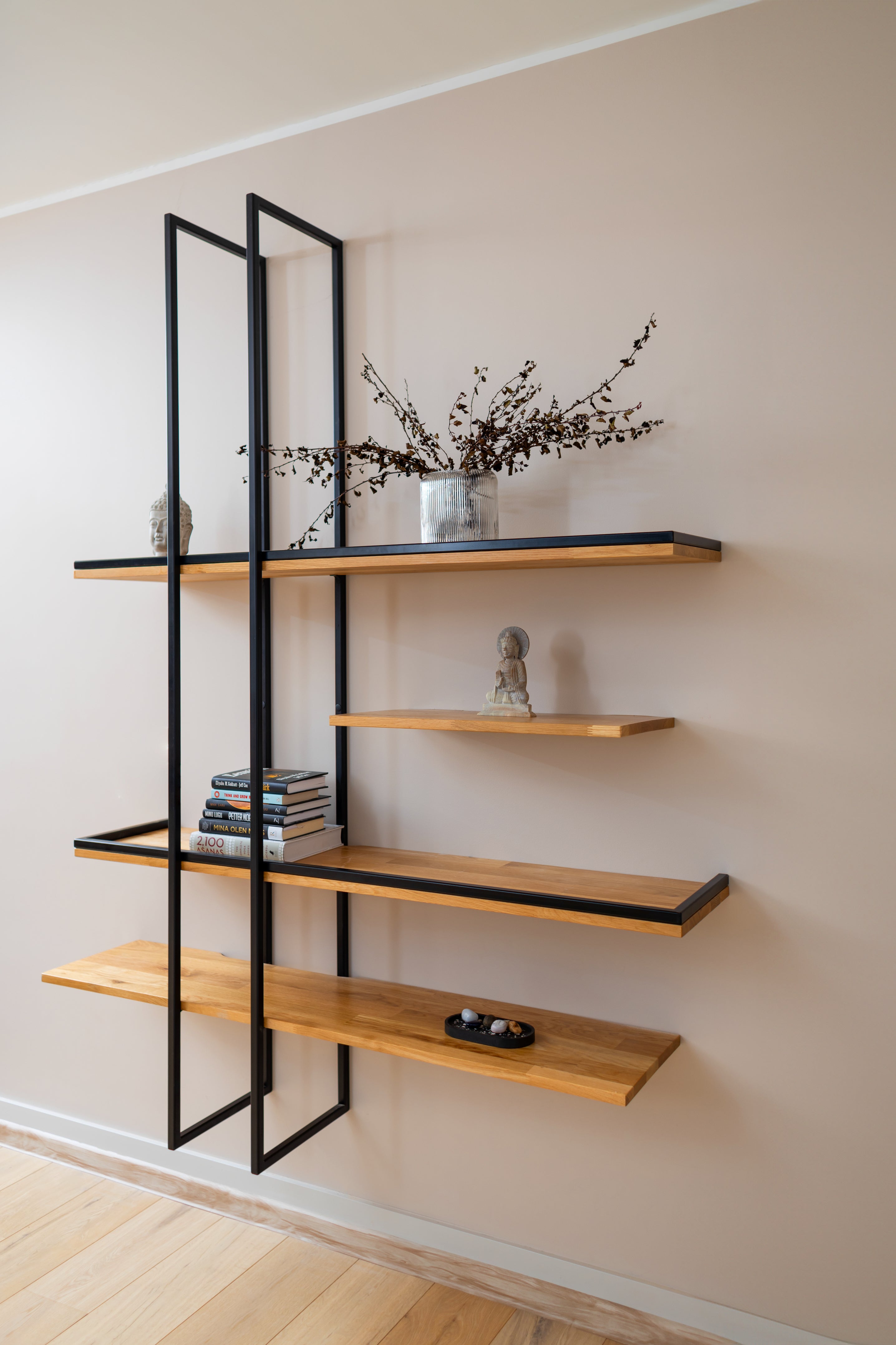 Solid wood floating shelf PÄIKE with two metal frames on a living room wall decorated with a plant and books